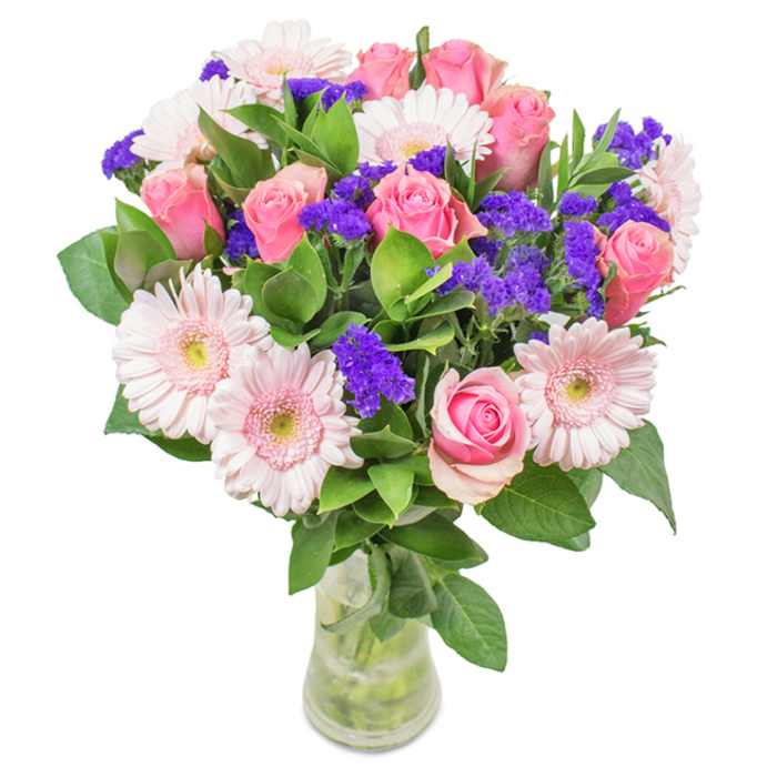 A visually stunning floral arrangement, expertly crafted in Thornton Heath and presented in a clear, elegant glass vase against a crisp white backdrop. The bouquet's centerpiece features approximately seven to nine soft and medium pink roses, each bud unfurling or poised to bloom in that classic spiral form beloved by local flower enthusiasts. These are harmoniously paired with five to seven pale pink gerbera daisies, whose large, circular heads and radiating petals, blushed with lighter central discs, impart both a sense of innocence and warmth. Bright clusters of purple statice, serving as playful filler flowers, add pronounced texture and a deep pop of color within the bouquet, while lush foliage in vivid green cascades around the blooms, conjuring the richness of Thornton Heath's green spaces. The transparent vase showcases the fresh-cut stems and sparkling water, epitomizing the freshness and quality typical of same-day flower delivery in the area. Suitable for special occasions from anniversaries along Beulah Road to Mother's Day or heartfelt celebrations, this graceful bouquet reflects the joy and affection cherished by the Thornton Heath community.