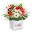 Bursting with local charm and uplifting colour, this stunning bouquet feels like a celebration of Thornton Heath's own vibrant spirit, ready to brighten someone's day. Inside a spotless square white gift bag, ruffled carnations in shades of coral, peach, and red mingle joyfully, their rich petals echoing the lively blooms seen in nearby residential gardens. White daisies, with joyful green-gold centres, sit amongst the arrangement, radiating optimism like a warm morning by Thornton Heath's Trumble Gardens. Subtle sprays of baby's breath bring a cloudlike softness, weaving delicately through the blossoms, while hints of tightly furled purple buds add hidden intrigue along the arrangement's edge. Deep, shiny green foliage fans outward, cloaking the bouquet in a natural embrace and creating a lush, rounded silhouette that feels both abundant and inviting. The white gift bag, fitted with sturdy white ribbons for easy carrying, elevates the presentation, perfect for gifting on special occasions-from birthdays and anniversaries to moments of heartfelt kindness shared along Brigstock Road. Framed by a clean white background, every detail-colour, texture, and expert composition-comes alive, telling a story of freshness and thoughtful craftsmanship from a trusted local florist. Florist Thornton Heath's passion and artistry shine in each carefully chosen stem, making this bouquet a truly memorable gesture for any treasured recipient in the community.